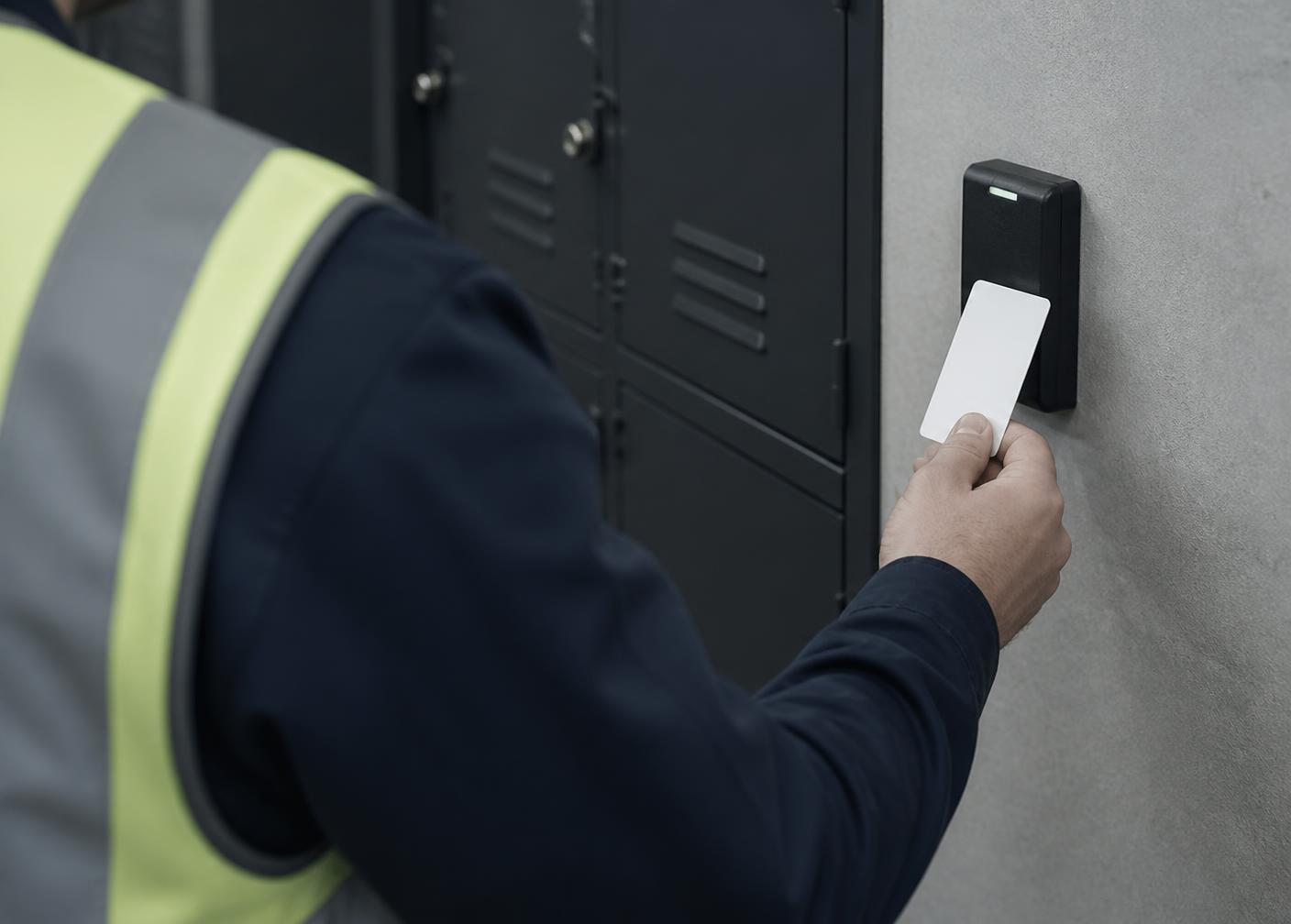 Worker in a hi-vis vest tapping a badge on a wall-mounted reader beside a bank of lockers